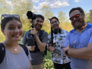 Four people smiling for a selfie with production equipment while shooting material for giving week