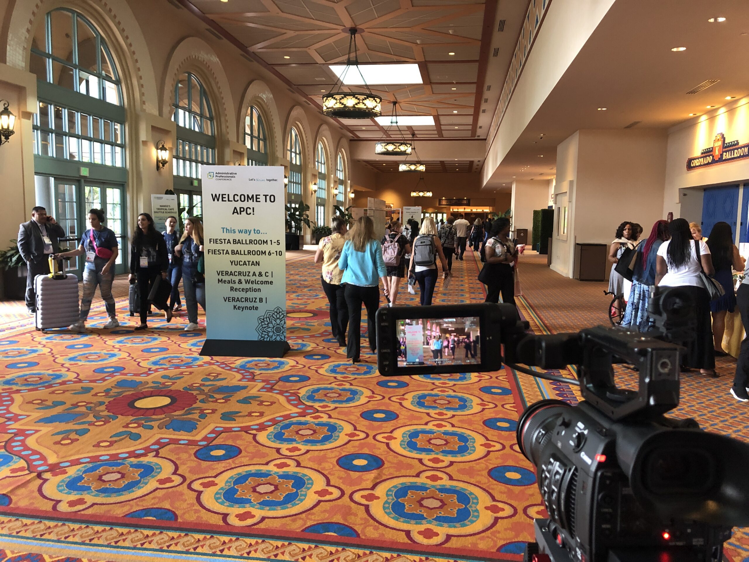 A camera is set up filming as people walk down a hallway