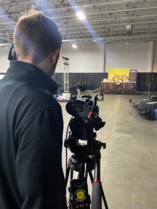 Camera person films side stage at a conference for digital live streaming audience