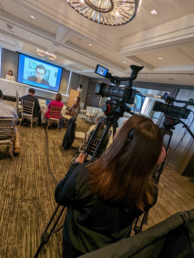 Woman standing behind a camera filming a hybrid event