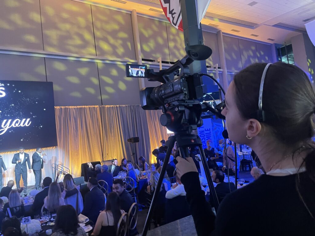 Woman behind camera pointing at stage at an event